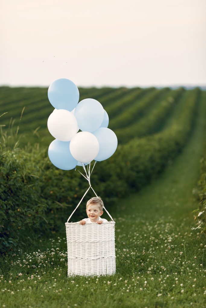 Little child sitting in the basket with balloons